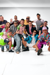 Fotografía de estudio en plano entero de los doce integrantes de la banda argentina Los Caligaris posando con actitud divertida y vestimentas coloridas, incluyendo camisetas de fútbol, sombreros y chaquetas deportivas sobre un fondo blanco.
